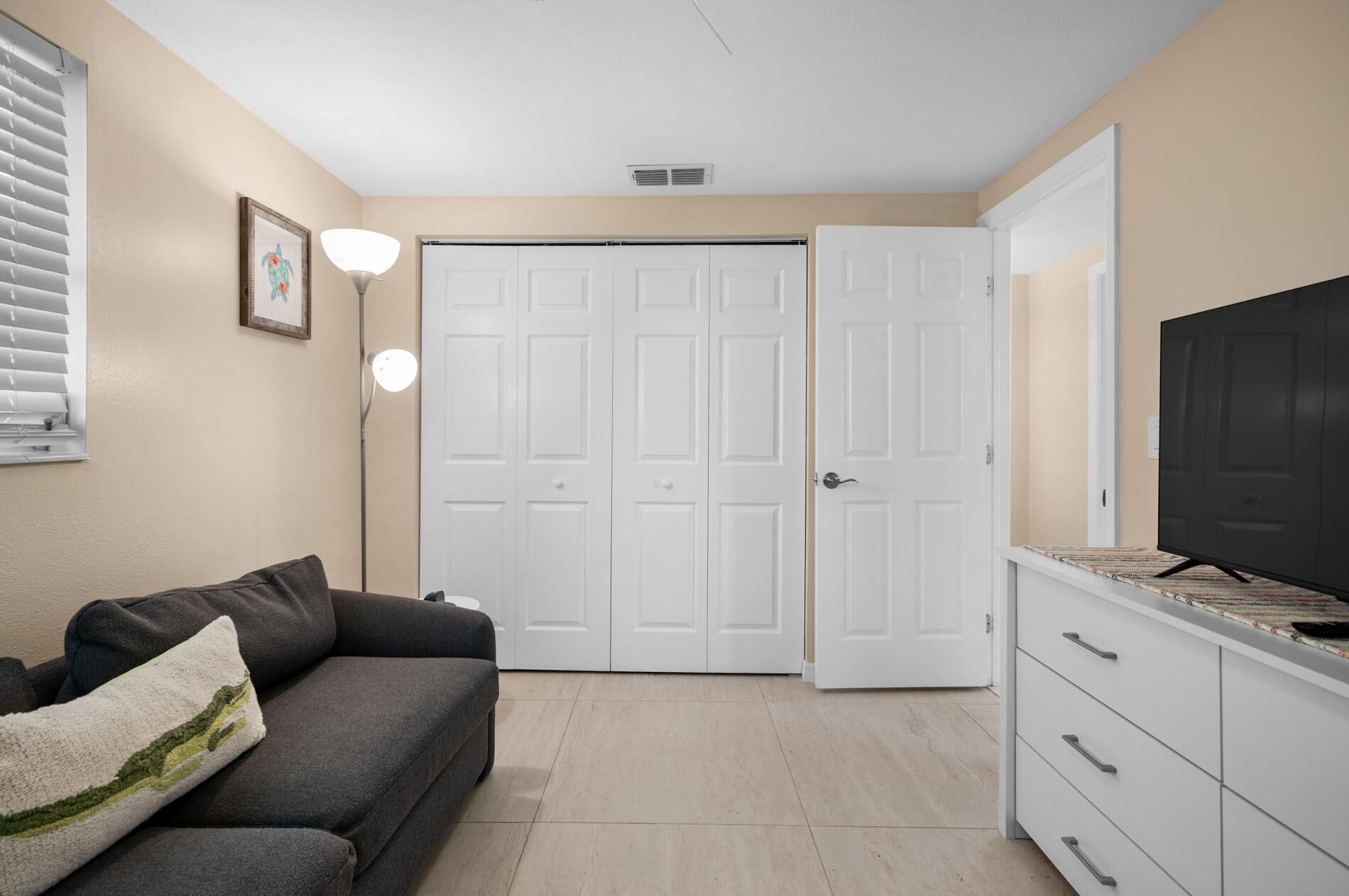 Una habitación con un sofá gris, un televisor sobre un mueble y puertas blancas.