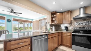 A modern kitchen with wooden cabinets, stainless steel appliances, and a large island with a dishwasher. - Waterfront 3BR – Pool, Dock, Kayaks & Beach (Englewood)