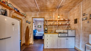 Eine kleine Küche mit Holzausbau, einem weißen Kühlschrank und einem Herd. Eine Holztür führt in einen anderen Raum.