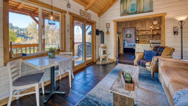 Ein gemütliches Blockhaus-Interieur mit Essbereich, Wohnzimmer mit Sofa, Küchenzeile und Blick ins Freie.