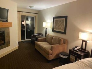Ein Hotelzimmer mit einer Couch, einem Fernseher, einem Schreibtisch mit Lampe und einem gerahmten Bild an der Wand.