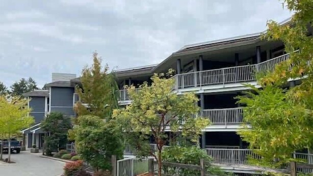 A multi-story residential building with balconies, surrounded by mature trees and a paved street.