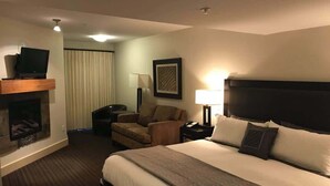 A hotel room with a large bed, a fireplace, a sofa, a desk, and a television.