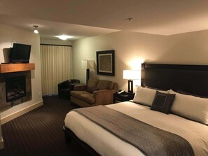A hotel room with a large bed, a fireplace, a sofa, a desk, and a television.