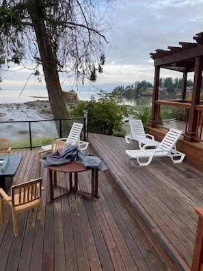 A wooden deck with a table and chairs, overlooking a body of water and a forested area.
