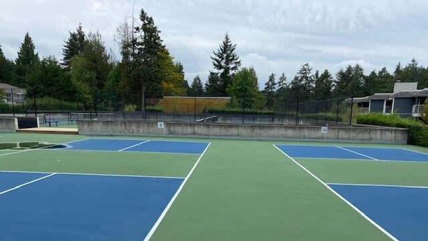 An outdoor tennis court with multiple courts, surrounded by trees and a fence.