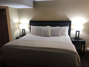 A neatly made bed with a dark headboard, two bedside tables with lamps, and a door on the left.