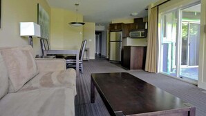 A modern living room with a sofa, a coffee table, and a dining area with a table and chairs. There is a kitchen area with cabinets and appliances.