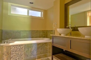 A bathroom with a bathtub, two sinks, and a large mirror.