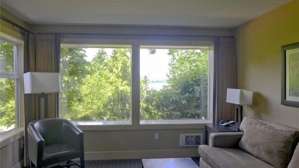 A room with a large window, a chair, a sofa, and a lamp. - Estuary Escape - 1BDRM - Full Kitchen (Nanoose Bay)