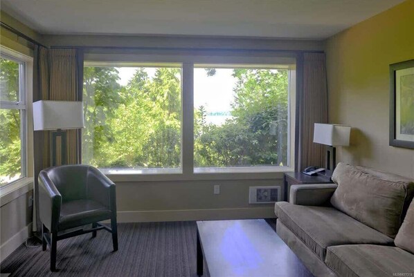 A room with a large window, a chair, a sofa, and a lamp.