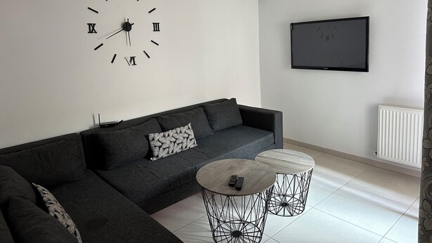 A modern living room with a sectional sofa, a round coffee table, a wall clock, an air conditioning unit, and a flat-screen TV. - Luxury apartment  (Ariana)