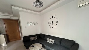 A modern living room with a grey sofa, two round coffee tables, a large wall clock, and a decorative ceiling light. - Luxury apartment  (Ariana)