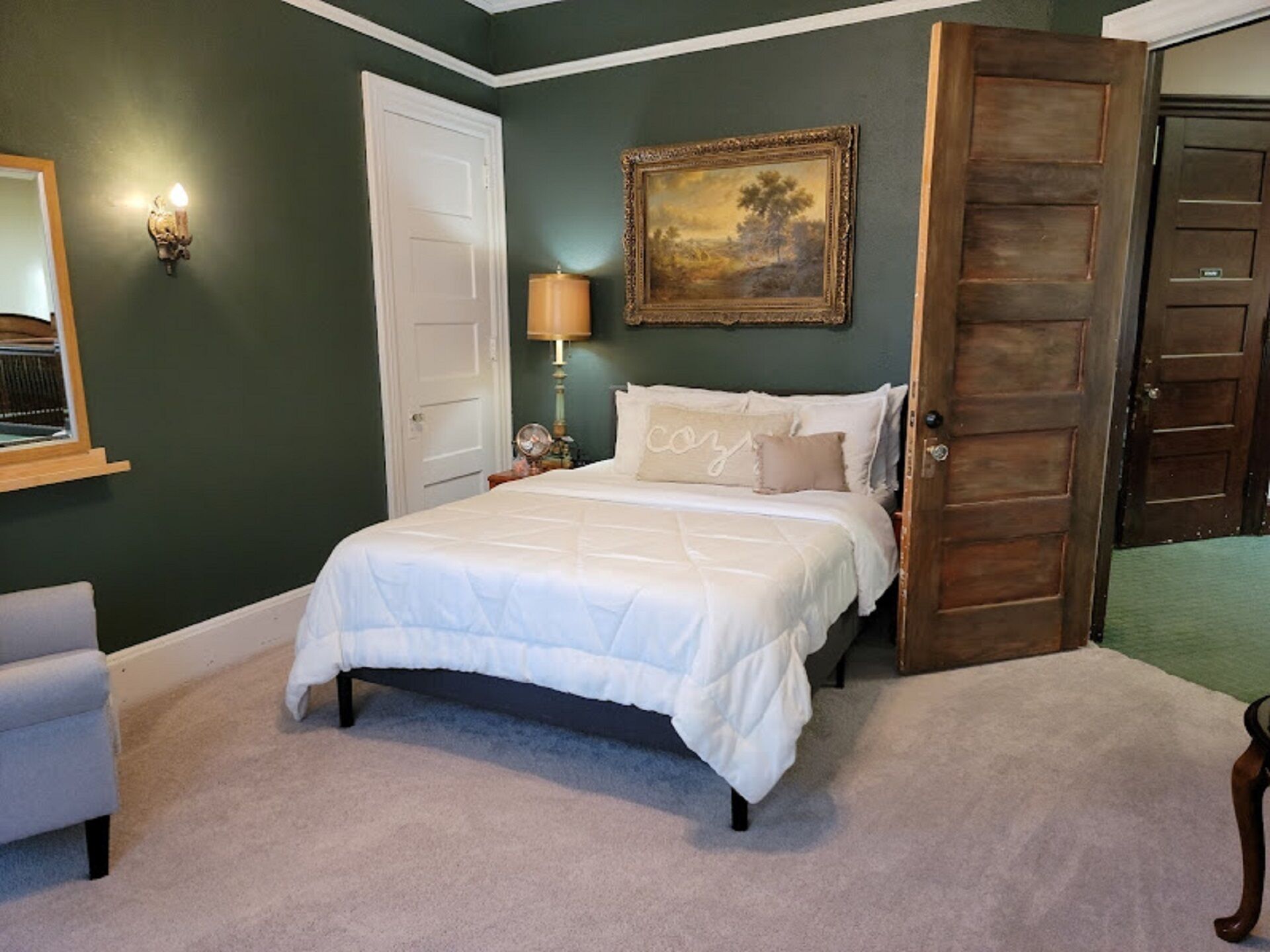 A bedroom with a bed, a nightstand, a lamp, a door, and a painting on the wall.