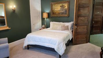 A bedroom with a bed, a nightstand, a lamp, a door, and a painting on the wall.