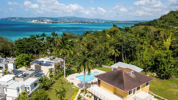 Zona residencial com painéis solares nos telhados, piscina e vegetação exuberante.