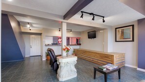 A reception area with a bench, a table, a potted plant, a leather chair, and a television mounted on the wall. - Capital O 3Y Motel Mount Vernon Renfro Valley (Mount Vernon)
