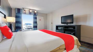 A hotel room with a large bed, a television, a desk with a lamp, and a view of the outside.