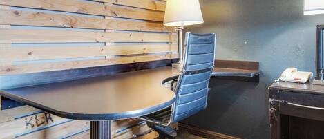 Un salón de conferencias con un muro de listones de madera, una silla de oficina azul, un escritorio con una lámpara y un teléfono sobre una pequeña mesa.