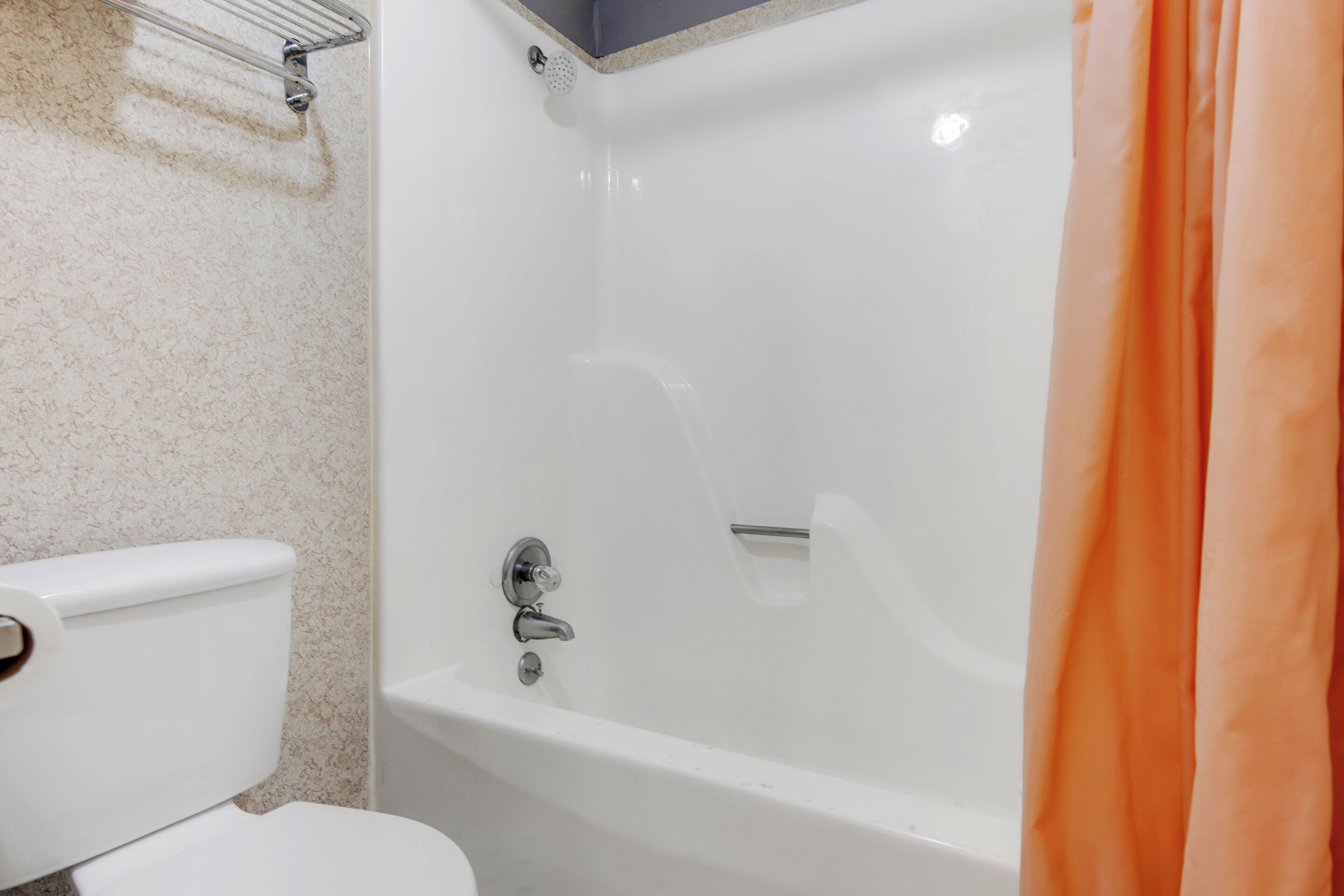 A bathroom with a white toilet, a bathtub, and an orange shower curtain.