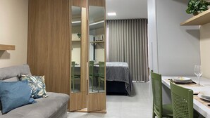 A modern room with a grey sofa, a wooden wardrobe, a dining table with chairs, and a bed with a grey bedspread. - Bela Hospedagem - Neo Duos 104 (Cabedelo)