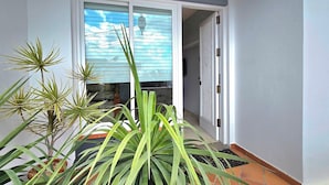 Un balcón con plantas en macetas, una puerta corrediza de vidrio que da a una habitación y una lámpara colgante.