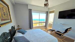 Habitación de hotel con una cama grande, una silla, televisión y balcón con vista al mar.