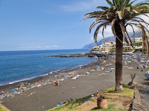 A beach with people sunbathing and swimming, palm trees, and buildings in the background. - Home2Book Seaside Escape Playa La Arena (Puerto Santiago)