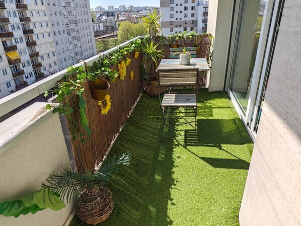 A balcony with artificial grass, a wooden table, and potted plants. - In the hanging garden  (Vanves)