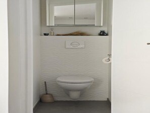 A small, modern bathroom with a toilet, a hand dryer, and a mirror above the sink. - In the hanging garden  (Vanves)