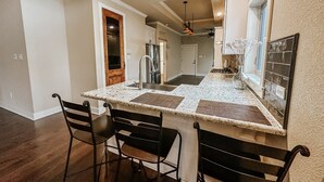 Cozinha com ilha central, dois banquetes, geladeira e painel de azulejos.