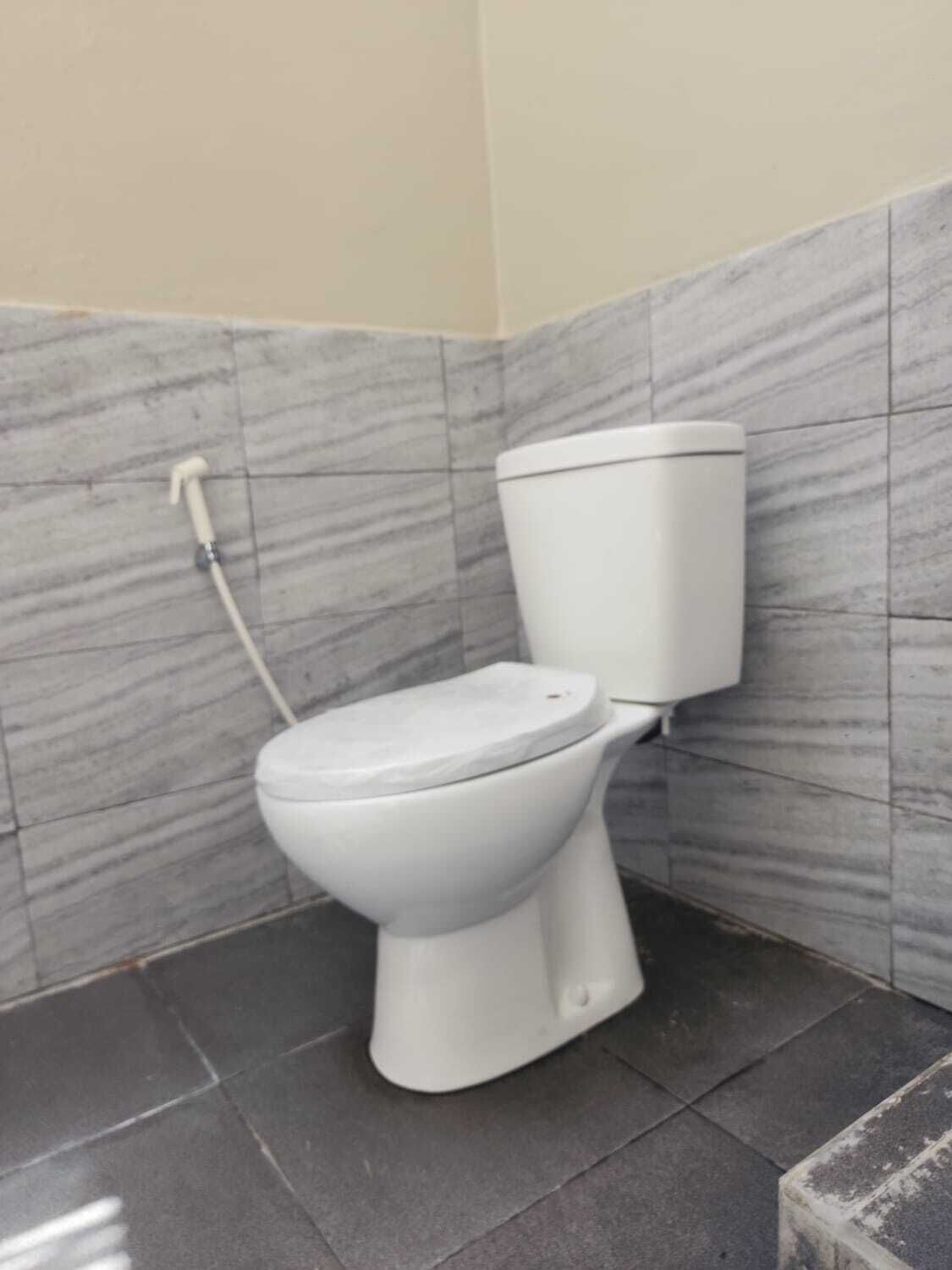 Des toilettes dans une salle de bain aux murs décorés d’un motif imitant le marbre et au sol recouvert de carreaux sombres.