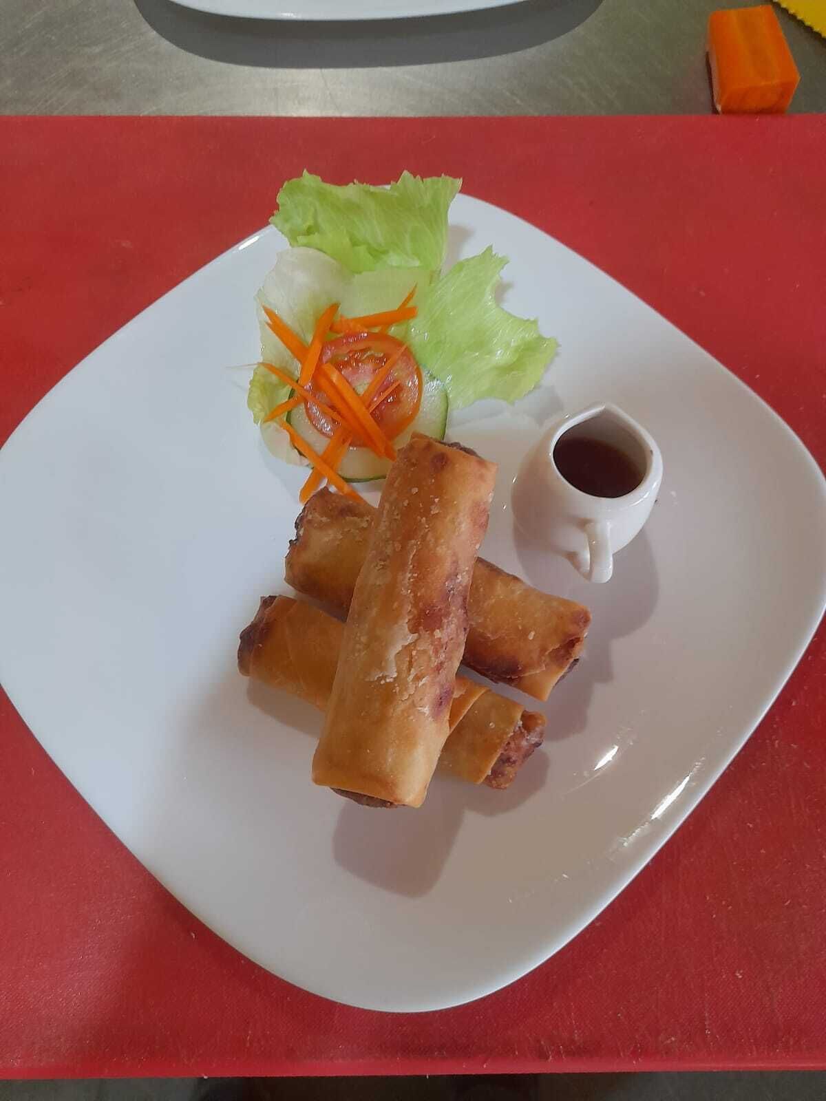 Une assiette contenant des rouleaux de printemps, de la laitue, des carottes râpées et une petite coupelle de sauce.