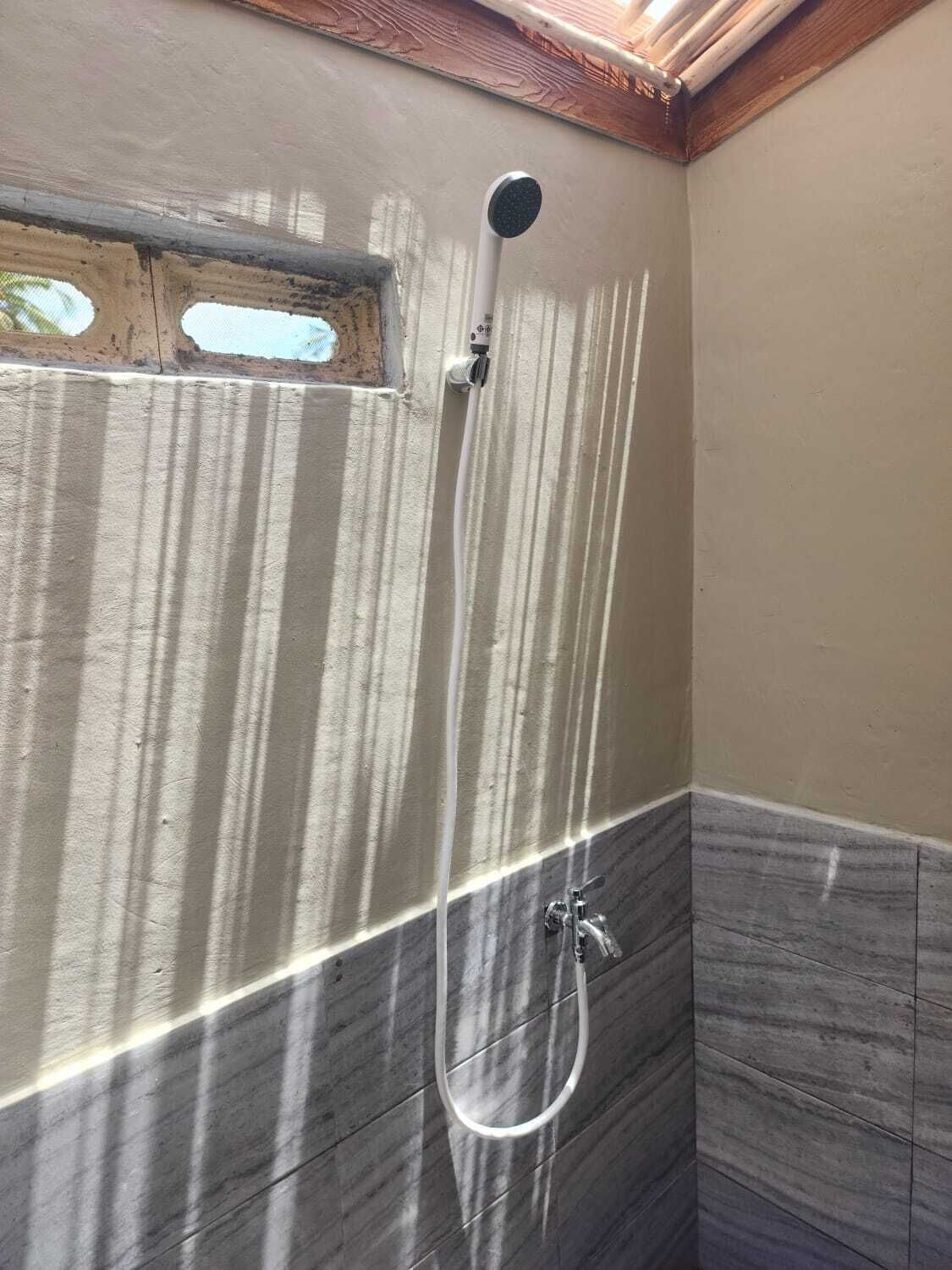A shower with a handheld showerhead and a handheld hose, a small window, and a corner with a tiled wall.