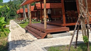 A wooden structure with a tiled roof, surrounded by palm trees and a clear sky. - Mio Villa Tomang Omang Lombok (Selong Belanak)