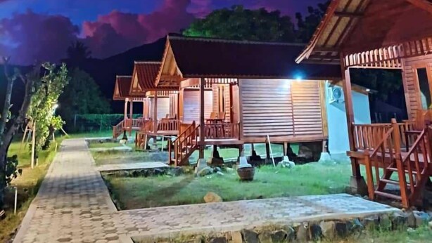 A row of wooden cabins with a paved pathway leading to them, set against a twilight sky. - Mio Villa Tomang Omang Lombok (Selong Belanak)