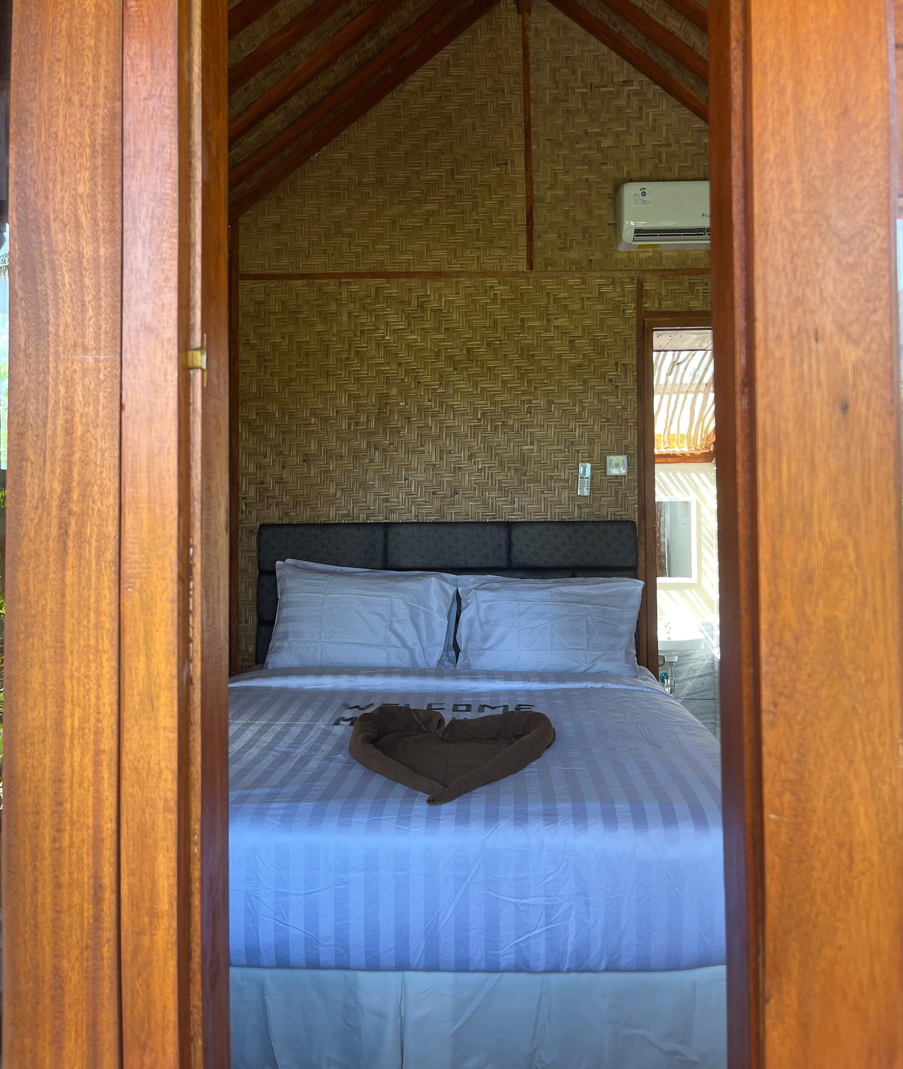 Una cama con un cojín con forma de corazón y un cartel que dice 'WELCOME', vigas de madera y un patrón tejido en la pared.