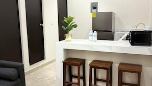 A small kitchenette with a refrigerator, microwave, and bar stools. There is a potted plant on the counter and a newspaper on the table. - Hortensias Hotel and Suites (Tapachula)