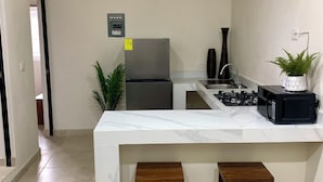 A modern kitchen with a marble countertop, two wooden stools, a refrigerator, a microwave, and a sink. - Hortensias Hotel and Suites (Tapachula)