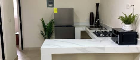 Una cocina moderna con encimera de mármol, dos taburetes de madera, un refrigerador, un microondas y un lavamanos.