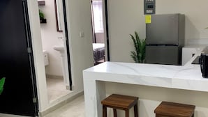 A kitchen with a white countertop, two wooden stools, a refrigerator, and a potted plant. - Hortensias Hotel and Suites (Tapachula)
