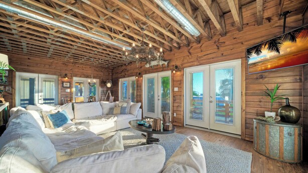 A spacious living room with a wooden ceiling, a large sofa, a coffee table, and a decorative vase. - Fish Camp by Avantstay Unique Escape, Pool + Views! (Port Aransas)