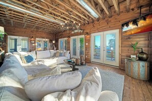A spacious living room with a wooden ceiling, a large sofa, a coffee table, and a decorative vase. - Fish Camp by Avantstay Unique Escape, Pool + Views! (Port Aransas)