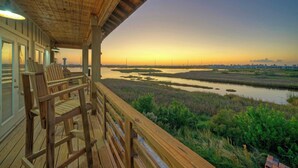 A wooden deck with chairs overlooking a marshy landscape during sunset. - Fish Camp by Avantstay Unique Escape, Pool + Views! (Port Aransas)