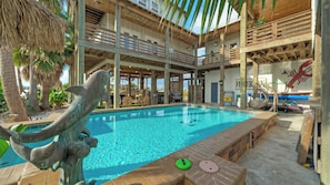 A pool with a dolphin sculpture, a wooden deck, and a view of the ocean.