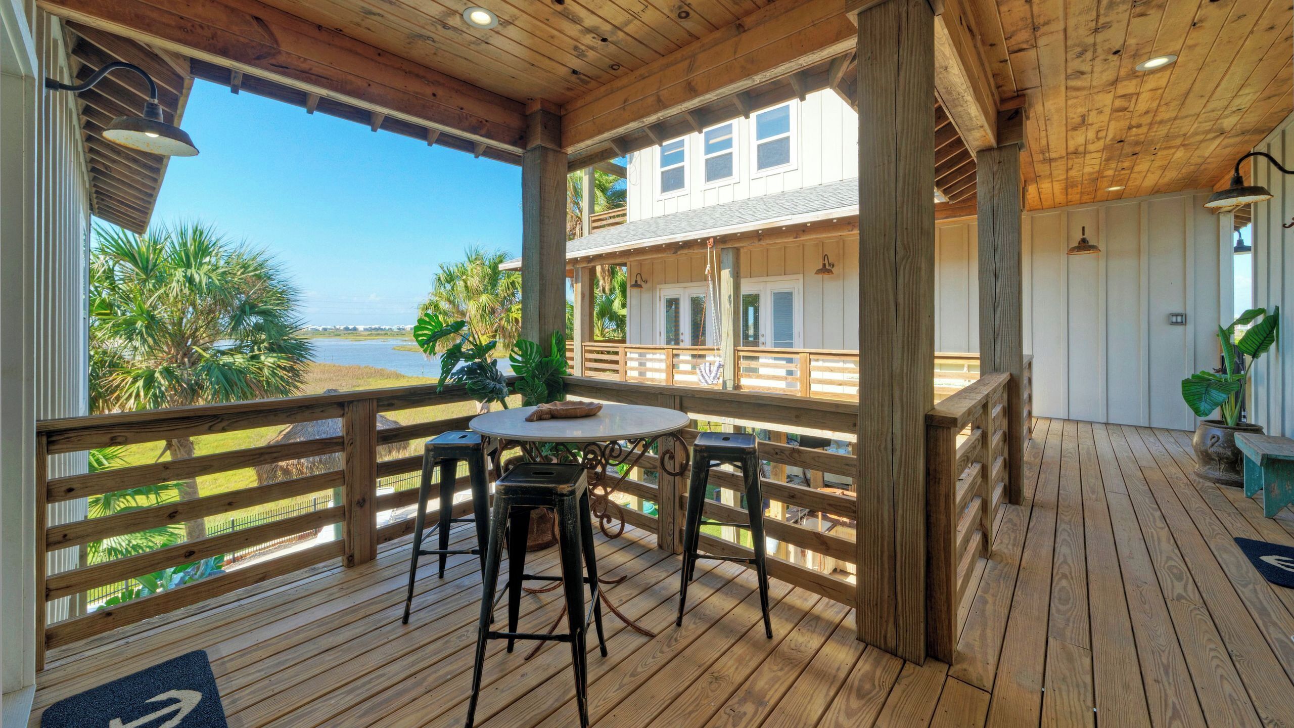 A wooden deck with a table and chairs, overlooking a body of water and palm trees.