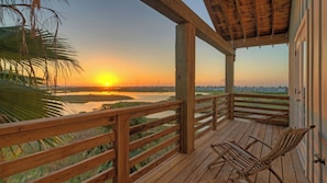 A wooden deck with a view of a sunset over a water body, a boat storage sign, and a palm tree.