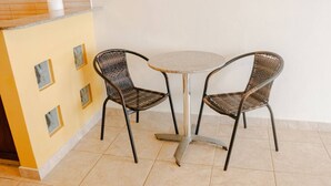 Un pequeño comedor con dos sillas de mimbre y una mesa redonda, una pared amarilla con una ventana y un cuadro colgado.