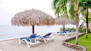 Un área de descanso en la playa con sombrillas de paja y sillas reclinables.