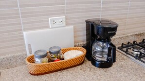 Una encimera de cocina con una cafetera, una cesta con frascos y un electrodoméstico blanco.